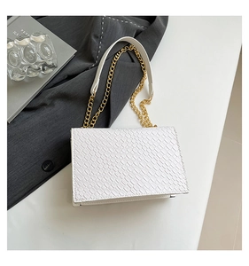 Detail shot of white faux crocodile textured bag with gold chain strap on grey blazer