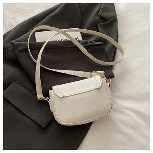 Detail of white litchi pattern leather crossbody bag with golden hardware on a grey blazer
