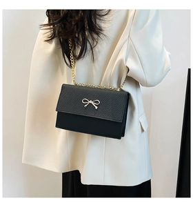Close-up of black leather crossbody bag with golden bow clasp on a white blazer