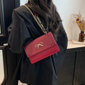 Elegant red chain shoulder bag with stone texture, gold bow buckle, and chain strap