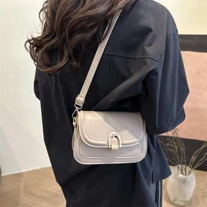Fashionable light grey saddle bag with golden horseshoe buckle worn as a shoulder bag