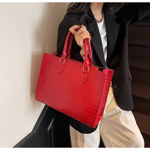 Detail of red crocodile textured tote bag with golden hardware and sturdy handles