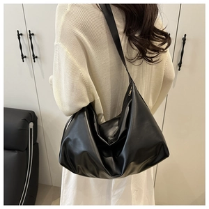 Close-up of a black matte leather tote bag worn by a model in a minimalist home setting