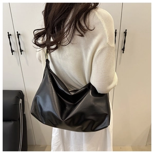 Detail view of a large black leather shoulder bag with gold metal rings on the strap