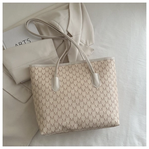 Close-up of beige tote bag with M-letter pattern on cream suit for stylish commute