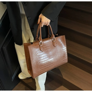 Detailed view of brown crocodile texture on a large tote bag held by a model