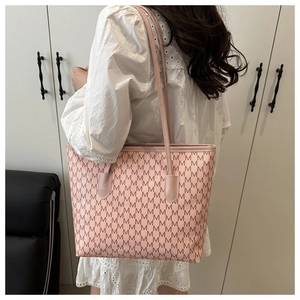 Pink faux leather tote bag featuring repeating M letter prints on a shoulder-worn model