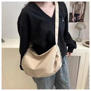 Detailed side view of a beige nylon crescent crossbody bag worn by a model in a minimal setting