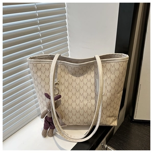 Detail of cream tote bag featuring monogram pattern and brown rabbit charm decoration
