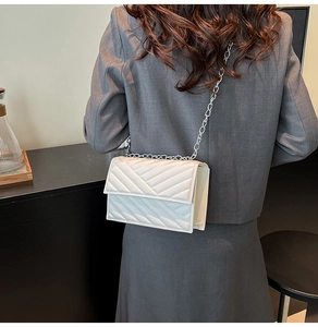 Détail d'un sac à rabat blanc avec motif matelassé en V et bandoulière chaîne argentée