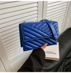 Détail d'un sac bandoulière bleu matelassé avec surpiqûres en V et chaîne argentée