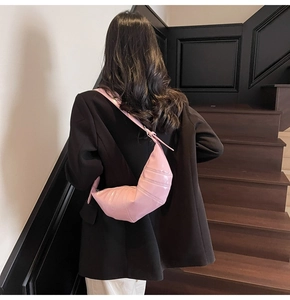 Detail of a pink croissant bag with pleated stitching worn by a model on a shoulder