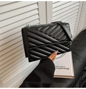 Détail du sac bandoulière en cuir matelassé noir avec chaîne argentée sur un canapé