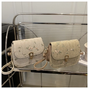 Detailed close-up of straw woven saddle bags with floral embroidery and golden u-lock