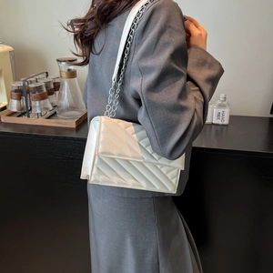 Sac à bandoulière matelassé blanc avec chaîne argentée porté par un mannequin en tailleur