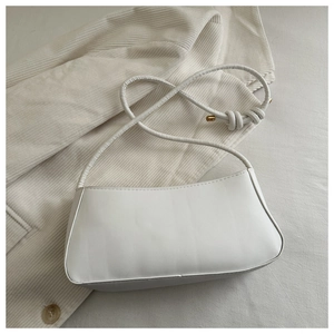 Detail of white minimalist PU leather underarm bag with knot strap and gold hardware accents