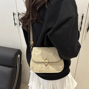 Beige straw saddle bag with floral embroidery and gold metal clasp on a female model