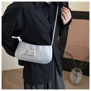Detail view of silver metallic bag with buckle strap worn by a model in a modern setting