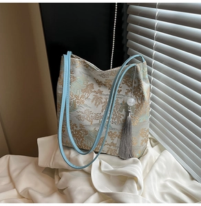 Close-up of golden Chinese landscape embroidery and grey tassel on a cream tote bag