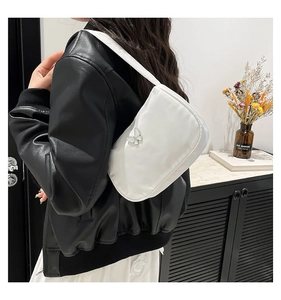 Close-up of white pleated underarm bag with silver butterfly buckle on black leather jacket