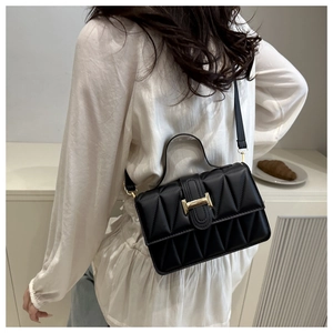 Détail du sac en cuir noir à motif géométrique et boucle dorée sur l'épaule du modèle