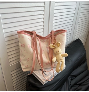 Detail view of white tote bag with pink cartoon prints and a cute rabbit plush pendant