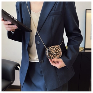 Detail view of mini leopard print crossbody bag with gold chain strap on a navy suit