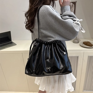 Glossy black drawstring bucket bag with silver bow accent on a shoulder strap
