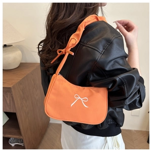 Close-up of bright orange baguette bag with white bow embroidery and knotted shoulder strap
