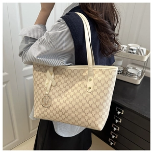 Detail view of beige monogram tote bag with gold M-logo charm and long shoulder straps