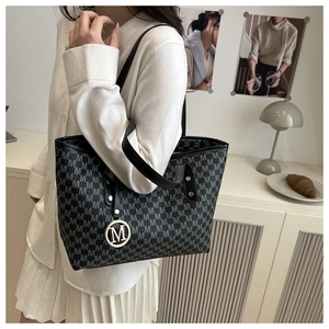 Side view of a black tote bag with silver M-letter monogram and golden logo charm