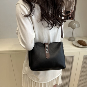 Minimalist black matte leather crossbody bucket bag with brown strap shown on a model