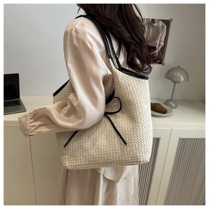 Detail of a beige woven tote bag with black contrast trim and a thin bow on the side