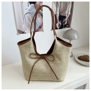 Detail of a straw tote bag with brown leather bow and contrasting trim on white desk