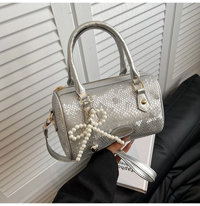 Close-up of silver snakeskin Boston bag with pearl bow charm and metal logo detail