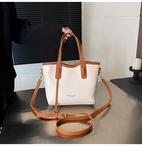 Detail of a chic cream leather bucket bag with brown handles and adjustable crossbody strap