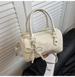 Detail of white snakeskin texture on a Boston bag with a pearl bow heart charm