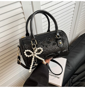 Close-up of black Boston bag with snake-skin embossing and pearl bow charm detail