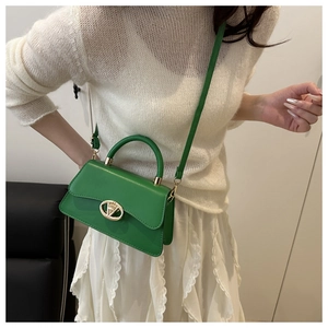 Detail of bright green trapezoidal handbag with gold circular logo and PU leather texture