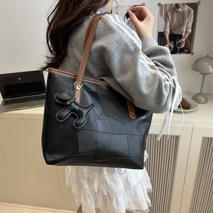 Black leather patchwork tote bag with brown straps and dog charm shown on shoulder