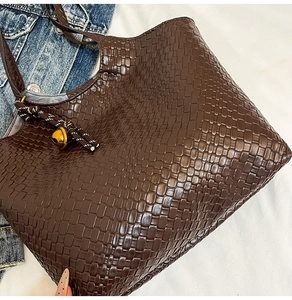 Détail d'un sac cabas en similicuir marron avec texture tressée et pendentif cloche dorée