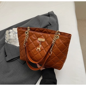 Detail of brown quilted tote bag with gold chain strap and a small deer charm