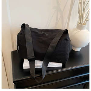 Détail du sac messager en nylon noir avec étiquette mode sur un décor minimaliste