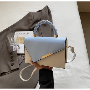 Dettaglio della borsa quadrata azzurra e beige con manico intrecciato e patta asimmetrica