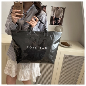 Large black glossy patent leather tote bag with white TOTE BAG text in a home setting