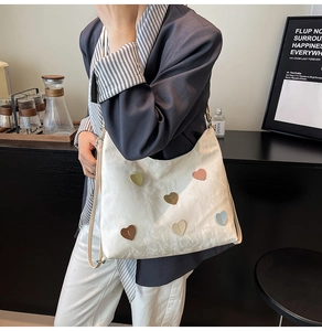 Detail of white pleated tote bag featuring five colorful heart patches and slim strap