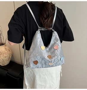 Silver pleated tote with colorful heart patches shown on model in a modern home setting