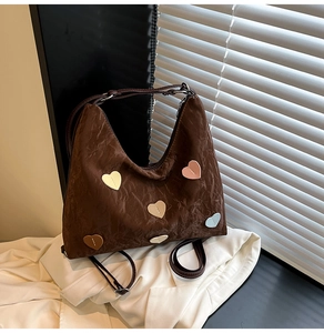 Close-up of brown pleated hobo bag featuring colorful heart patches on textured fabric