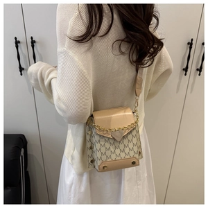 Detail of beige letter patterned crossbody bag with gold heart clasp and wide strap