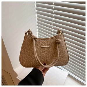 Close-up of tan woven texture underarm bag with knot strap and gold metal bar accent